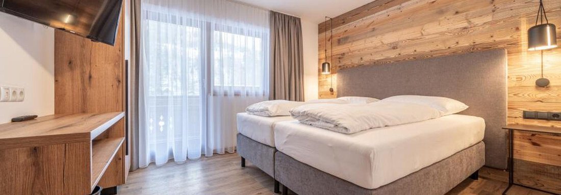 A modern bedroom with a double bed and wooden design. The room is bright and cozy, with a television and large windows. - Pension Miramonte - Sölden