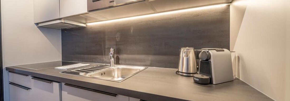 A modern kitchen with white cabinets and a gray workspace. The amenities include a sink, a microwave, and a kettle. - Pension Miramonte - Sölden
