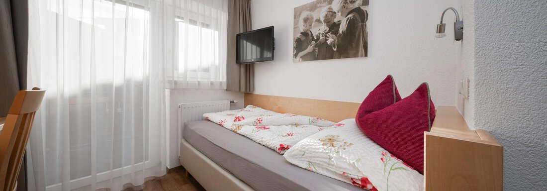 Einzelzimmer | © Andreas Ebermann, Pension Pitze (CC C) A small bedroom with a bed, decorated with cushions and pretty bedding. The room has large windows that let in a lot of daylight. - Pension Pitze - Sölden
