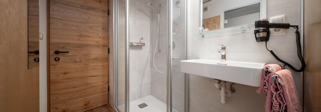 A modern bathroom with a glass shower and a simple sink. The wooden details create a cozy atmosphere. - Pension Pitze - Sölden