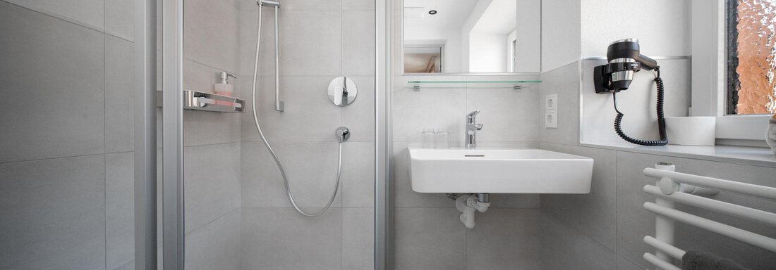 A modern bathroom with a shower cabin and a sink. The walls are tiled in light gray and there are natural light sources in the room. - Pension Pitze - Sölden