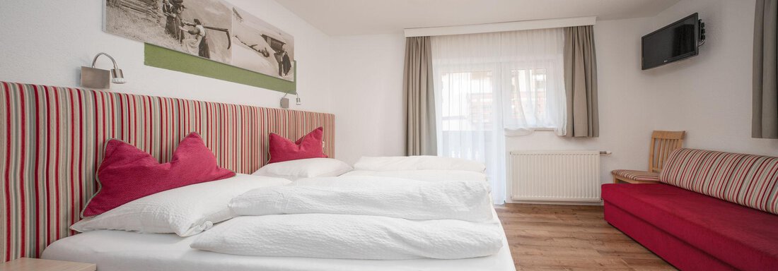 Dreibettzimmer | © Andreas Ebermann, Pension Pitze (CC C) A modern bedroom with two large beds and red pillows. There is a window with daylight and a red couch in the room. - Pension Pitze - Sölden
