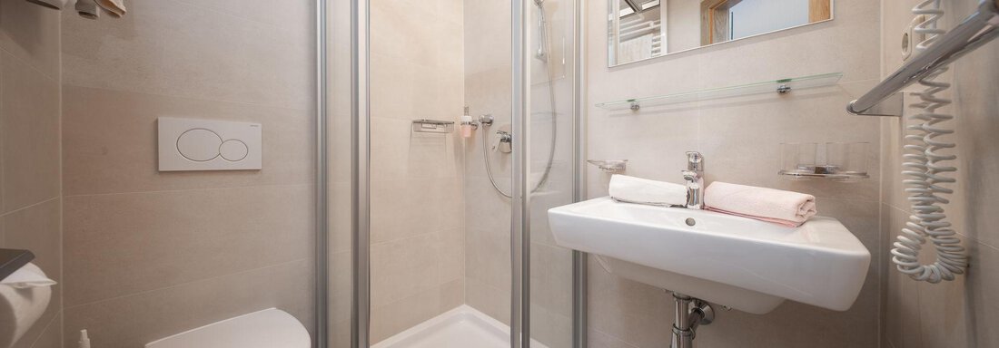 A modern bathroom with a shower, sink, and toilet. It is bright and clean, with neutral colors. - Pension Pitze - Sölden