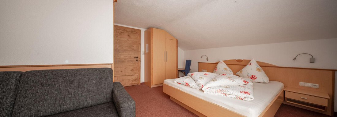 Vierbettzimmer | © Andreas Ebermann, Pension Pitze (CC C) A cozy bedroom with a double bed and a gray couch. The walls are light, and there is a wooden ceiling that creates a warm atmosphere. - Pension Pitze - Sölden