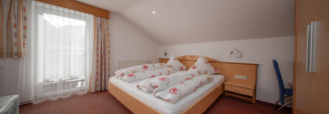 A cozy bedroom with a large bed and bright curtains. The room is simple and inviting, perfect for relaxing. - Pension Pitze - Sölden