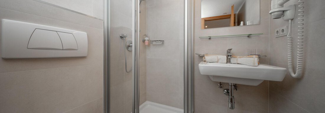 A modern bathroom with a shower area and a sink. The walls are bright and the fixtures are functional. - Pension Pitze - Sölden