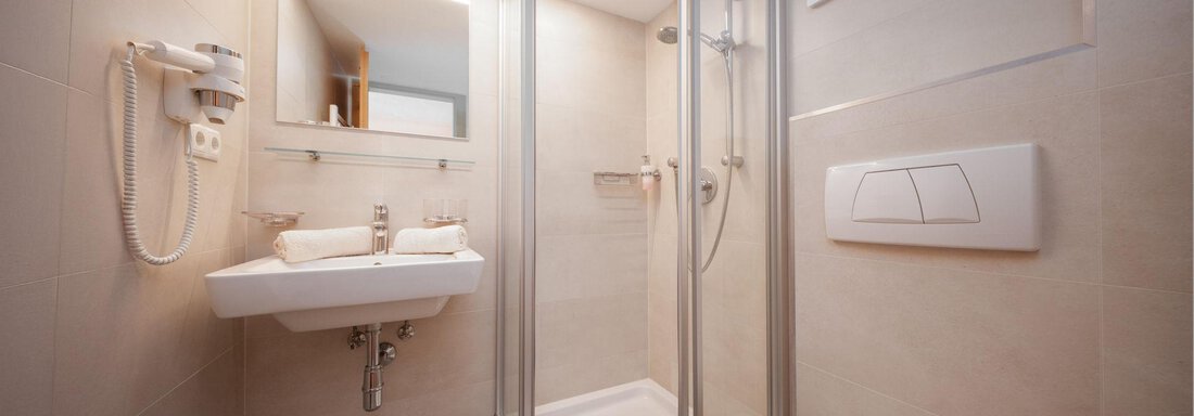 A modern bathroom with a glass shower and a sink. The walls are brightly tiled, and there is a toilet in the room. - Pension Pitze - Sölden