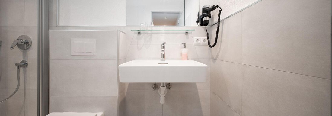 A modern bathroom with a shower, a sink, and a toilet. The walls are painted in neutral tones. - Pension Pitze - Sölden