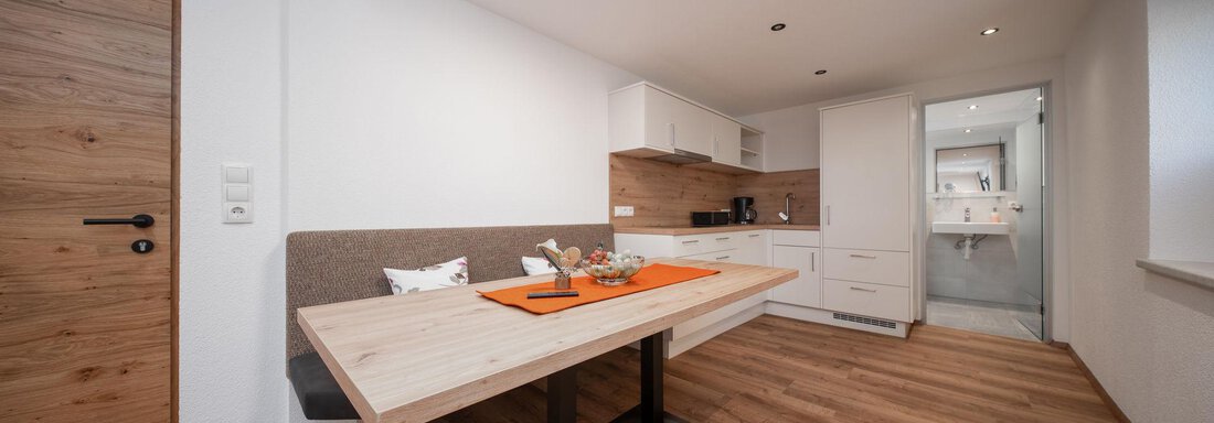 A modern kitchen with a large wooden table and a cozy seating area. The floor is made of wood, and there are bright walls as well as a well-equipped kitchenette. - Pension Pitze - Sölden