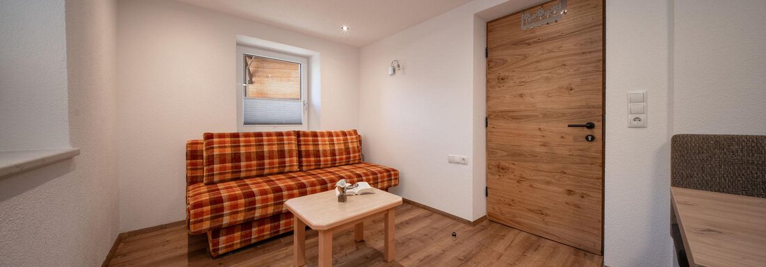 A cozy living space with a checkered sofa and a wooden table. Bright walls and a wooden floor create an inviting atmosphere. - Pension Pitze - Sölden
