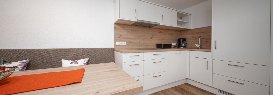 A modern kitchen with bright cabinets and wooden details. The dining area is cozy and inviting. - Pension Pitze - Sölden