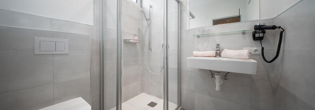 A modern bathroom with an enclosed shower and a sink. The walls are tiled in light gray and there are minimalist fixtures. - Pension Pitze - Sölden