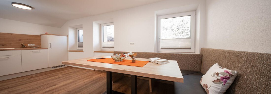 A modern dining room with a large table and comfortable seating. The walls are light, and the windows provide plenty of daylight. - Pension Pitze - Sölden