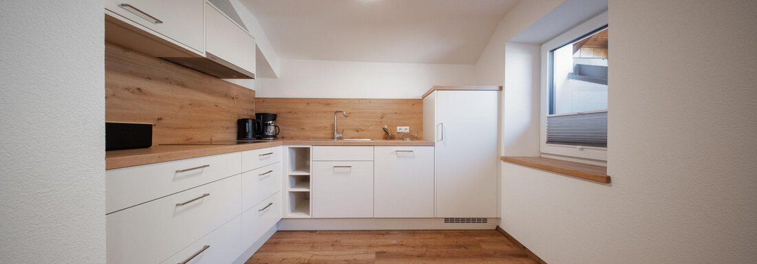 A modern kitchen with bright cabinets and wooden shelves. The floor is made of wood and the light is bright and inviting. - Pension Pitze - Sölden