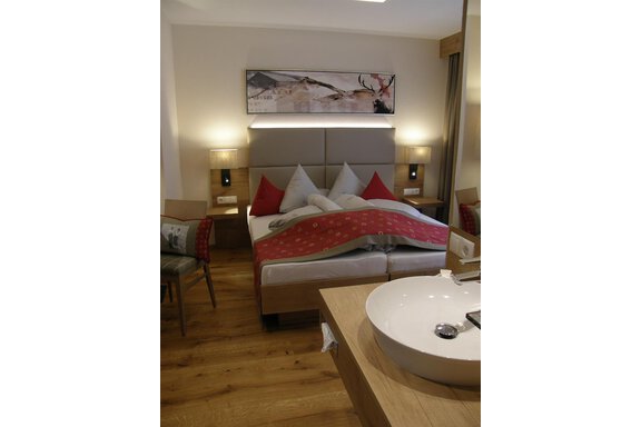 A modern bedroom with a double bed and red pillows. In the foreground, an elegant sink and wooden flooring can be seen. - Pension Sportalm - Sölden