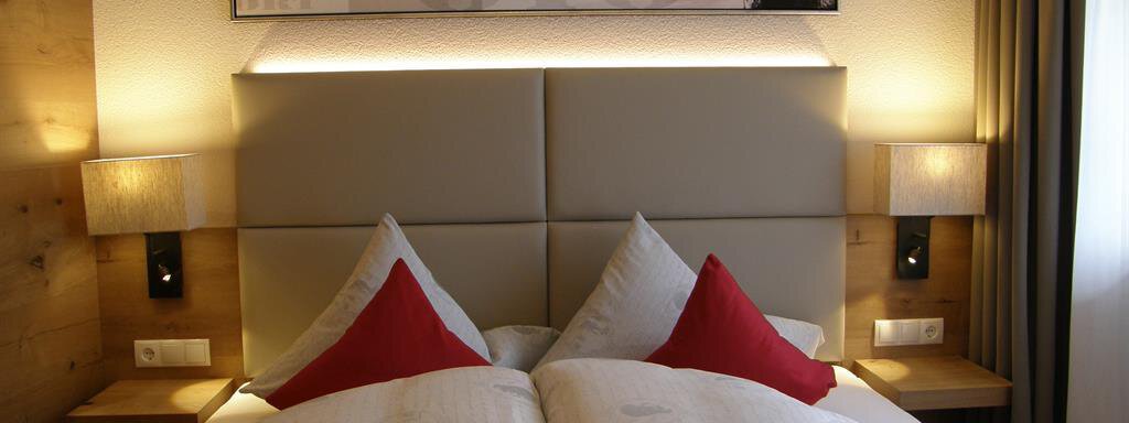 Doppelzimmer / Balkon A comfortable bedroom with a large bed and red pillows. The walls are light, and there is soft lighting from wall lamps. - Pension Sportalm - Sölden