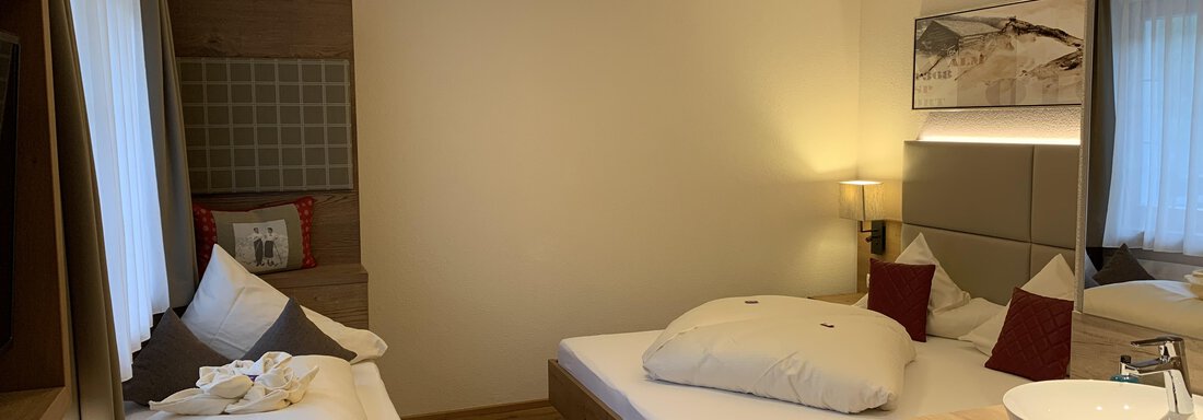 Dreibettzimmer A cozy bedroom with two beds and natural wood decor. The soft lighting creates an inviting atmosphere. - Pension Sportalm - Sölden