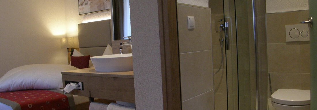 A cozy hotel room with a bed, a modern bathroom, and clean lines. The space is bright and invitingly designed. - Pension Sportalm - Sölden