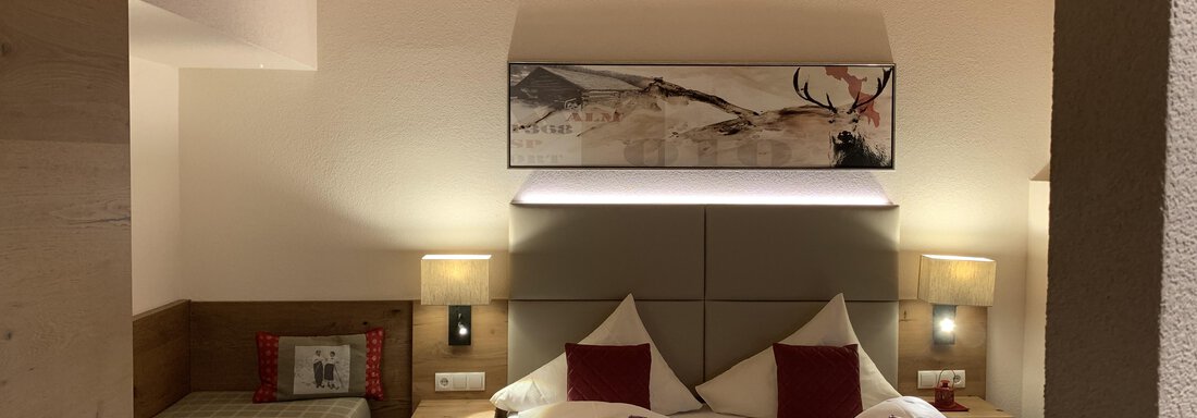 A cozy bedroom with a large double bed and two nightstands. A modern piece of art hangs on the wall, and there is an additional sleeping space on the left side. - Pension Sportalm - Sölden