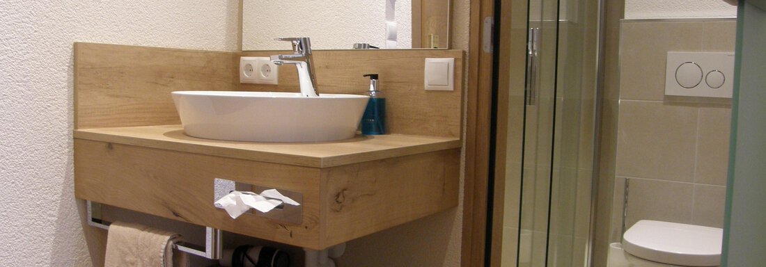 A modern bathroom with a wooden vanity and a sink. In the background, a shower and a toilet are visible. - Pension Sportalm - Sölden
