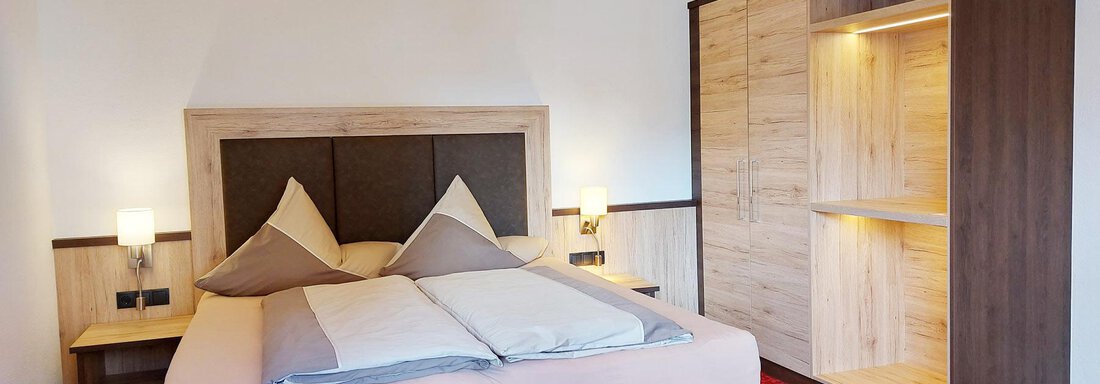 A cozy bedroom with a large bed and modern furniture. The carpet is red, and there are cabinets for storage. - Pension "Zur alten Mühle" - Sölden