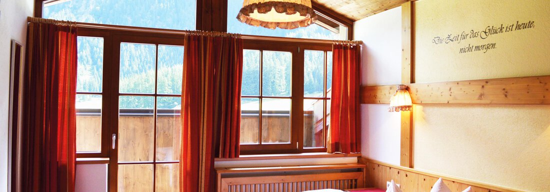 A cozy room with two beds and a large window. The wooden ceiling and warm light create an inviting atmosphere. - Pension "Zur alten Mühle" - Sölden
