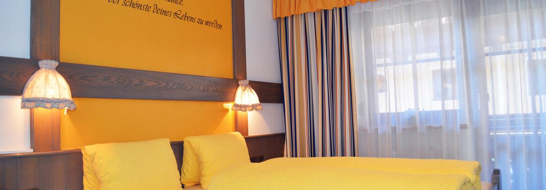 A bright room with yellow decor and a large window. The double bed has yellow bedding and there is modern lighting. - Pension "Zur alten Mühle" - Sölden