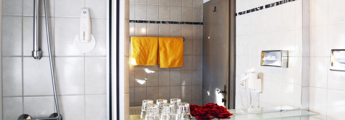 A modern bathroom with tiles and a large mirror. Towels in yellow and a small flower decoration create an inviting atmosphere. - Pension "Zur alten Mühle" - Sölden