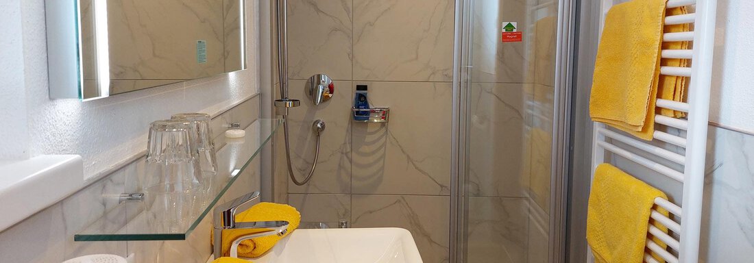 A modern bathroom with a shower and a sink. Yellow towels and glasses are decoratively arranged on the sink. - Pension "Zur alten Mühle" - Sölden