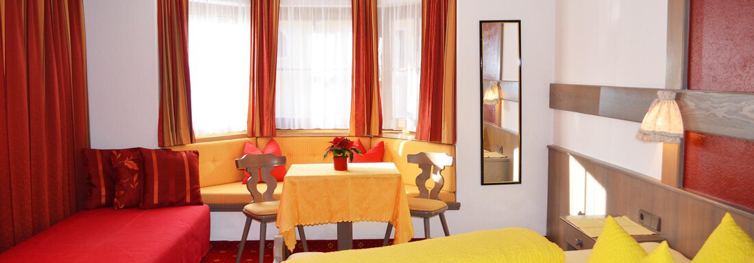 Family room A cozy room with a double bed and yellow pillows. There is a red sofa bed and a dining area with a table and chairs. - Pension "Zur alten Mühle" - Sölden