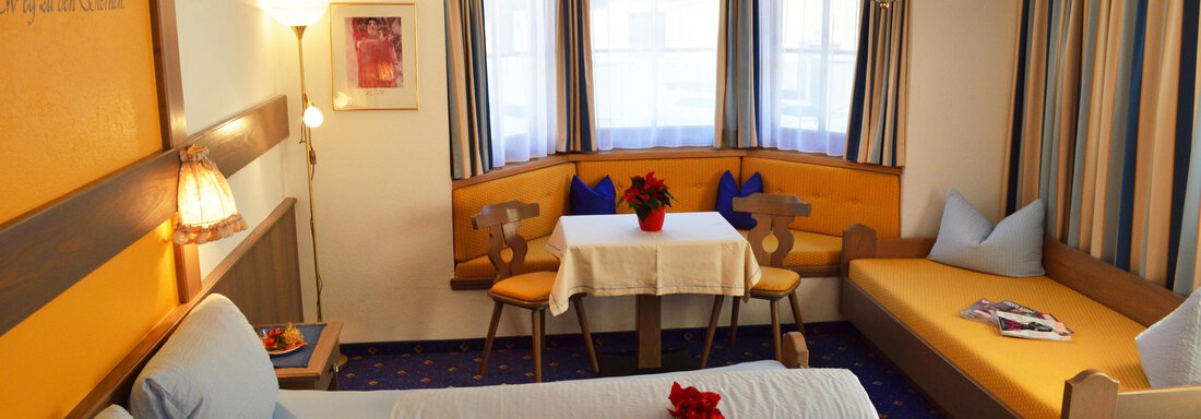 A cozy room with two beds, bright colors, and a dining area. Large windows provide plenty of daylight. - Pension "Zur alten Mühle" - Sölden