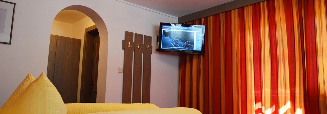 A cozy room with a large bed, yellow towels, and a television. The walls are painted in warm, striped colors. - Pension "Zur alten Mühle" - Sölden