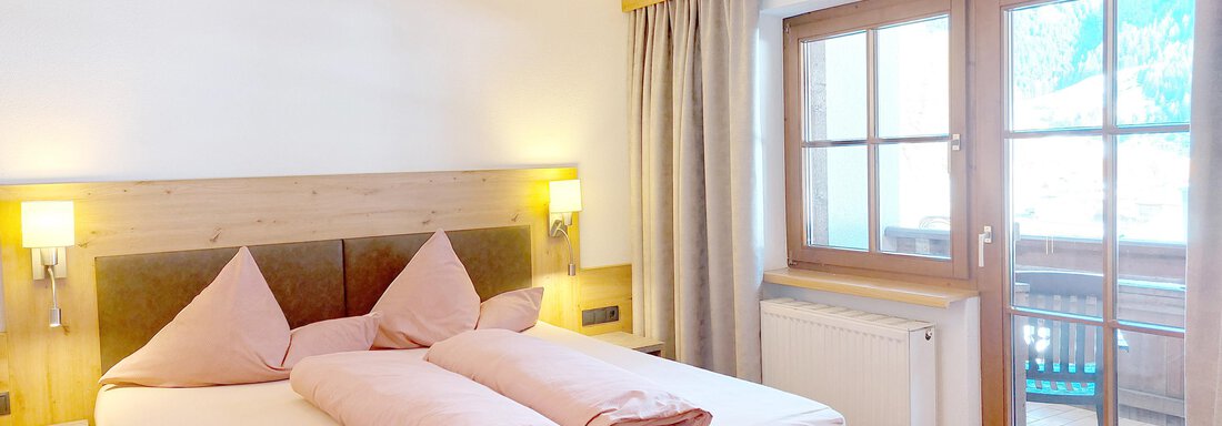 Apartment "small" A modern bedroom with a large bed and pink pillows. The room has large windows overlooking a balcony. - Pension "Zur alten Mühle" - Sölden