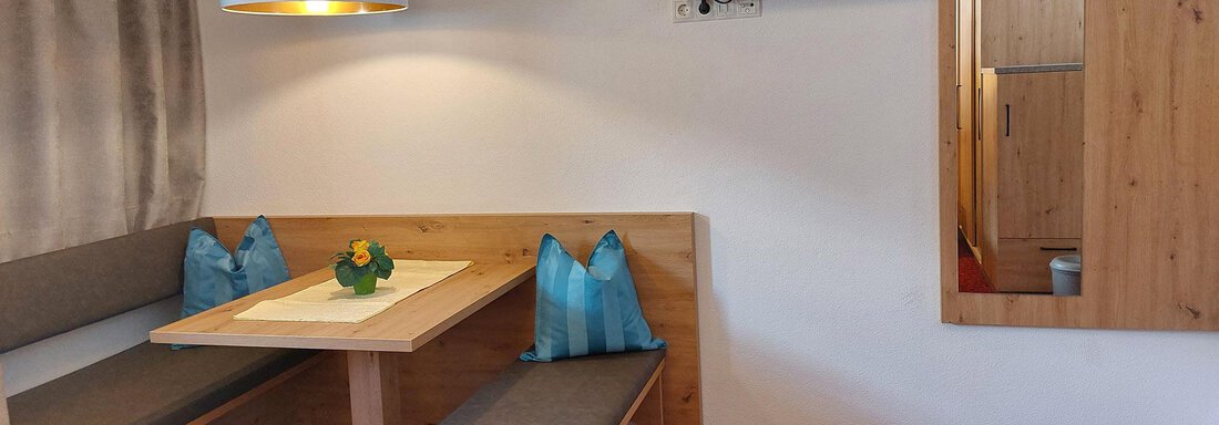 A cozy room with a table and benches made of wood. A television is mounted on the wall, and there is a mirror as well as a coat rack. - Pension "Zur alten Mühle" - Sölden