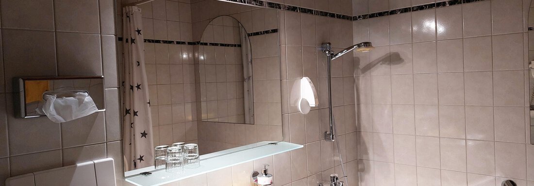 A modern bathroom with white tiles and a large mirror. The sanitary facilities are functional and clean, with yellow towels and a bathtub. - Pension "Zur alten Mühle" - Sölden
