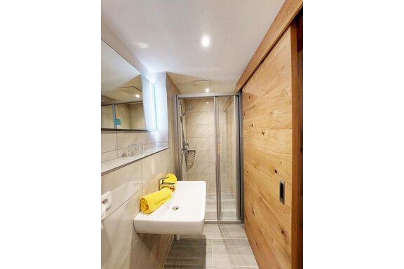 A modern bathroom with a shower and a sink. Yellow towels are neatly placed on the sink. - Pension "Zur alten Mühle" - Sölden