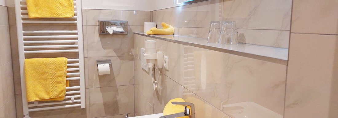 A modern bathroom with bright tiles and yellow towels. The room is well-lit and neatly furnished. - Pension "Zur alten Mühle" - Sölden