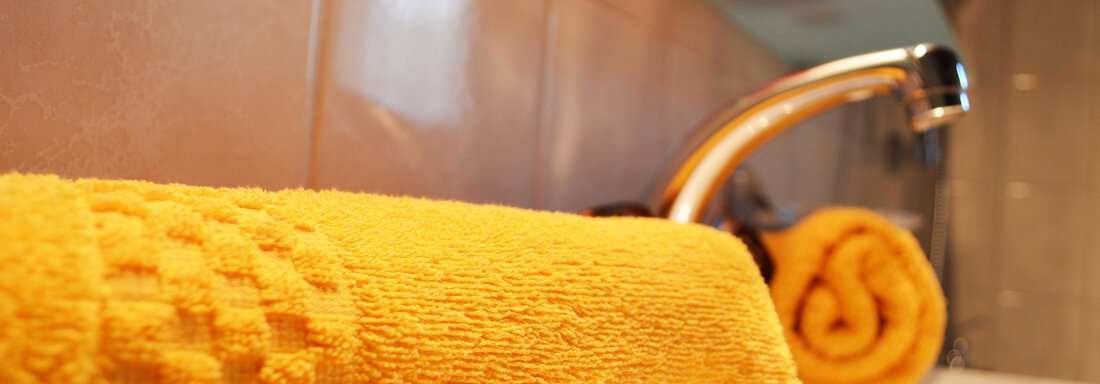A yellow towel lies next to a faucet in a bathroom. The background shows a modern, bright environment. - Pension "Zur alten Mühle" - Sölden