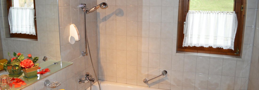 A modern bathroom with a bathtub and a shower. There are decorative towels and flowers on the sink. - Pension "Zur alten Mühle" - Sölden