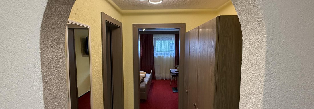 A bright hallway with elegant lamps and a red carpet. Mirrors and doors to other rooms can be seen on the left and right. - Pension "Zur alten Mühle" - Sölden
