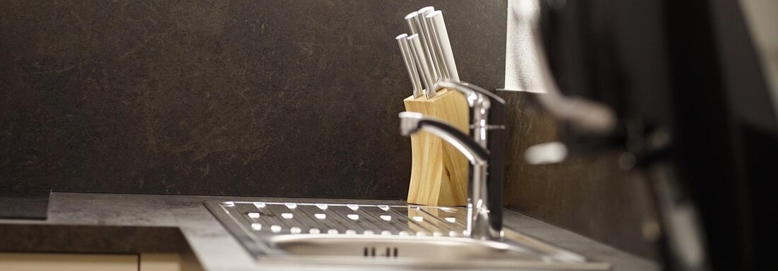 A modern kitchen area with a sink and a set of knives in a block. In the background, an elegant wall design can be seen. - Pension "Zur alten Mühle" - Sölden
