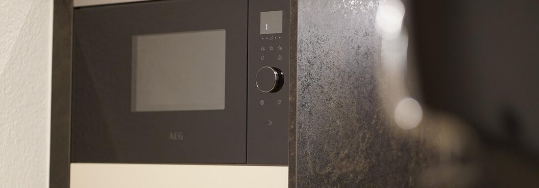 A modern microwave in a stylish kitchen unit. The surface is made of dark material with bright accents. - Pension "Zur alten Mühle" - Sölden