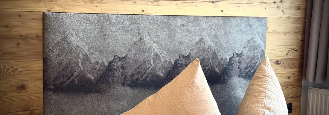 IMG_9700 A modern bedroom with wooden paneling and a headboard design that represents mountains. The two large pillows add a cozy touch. - Pension "Zur alten Mühle" - Sölden