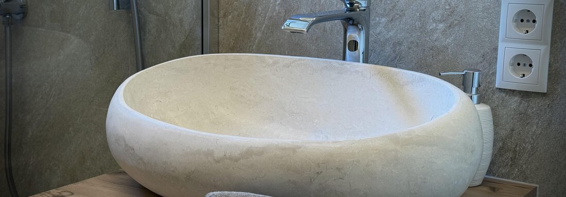 An elegant sink made of light stone is placed on a wooden base. Next to it lies a gray towel. - Pension "Zur alten Mühle" - Sölden