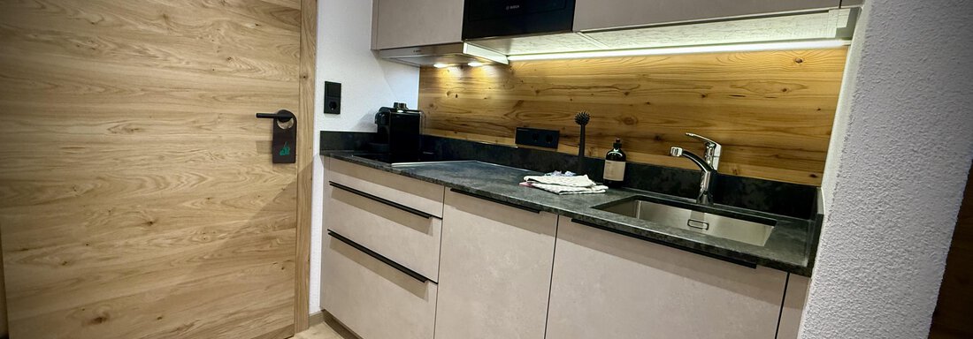 A modern kitchen with light wooden elements and black surfaces. It is well-equipped and offers a cozy atmosphere. - Pension "Zur alten Mühle" - Sölden