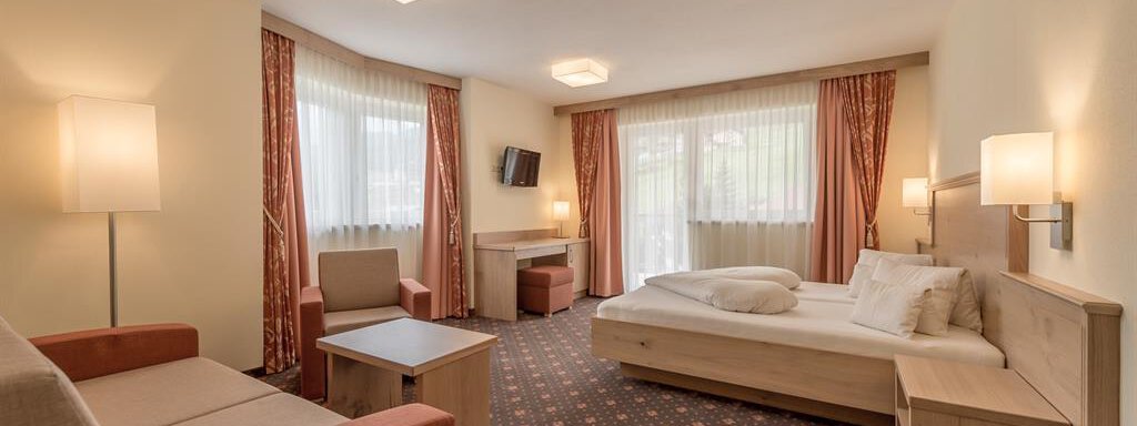 150728_143105-Bearbeitet | © AML (CC C) A comfortable hotel room with a large double bed, a seating area, and plenty of natural light. The decor is modern and cozy. - Residenz Allegra - Sölden