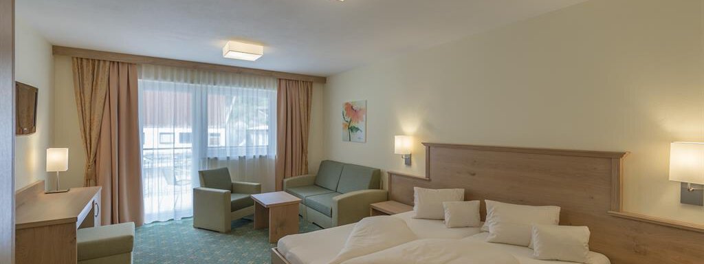 A cozy hotel room with a double bed, a sofa, and a table. Large windows provide plenty of daylight. - Residenz Allegra - Sölden