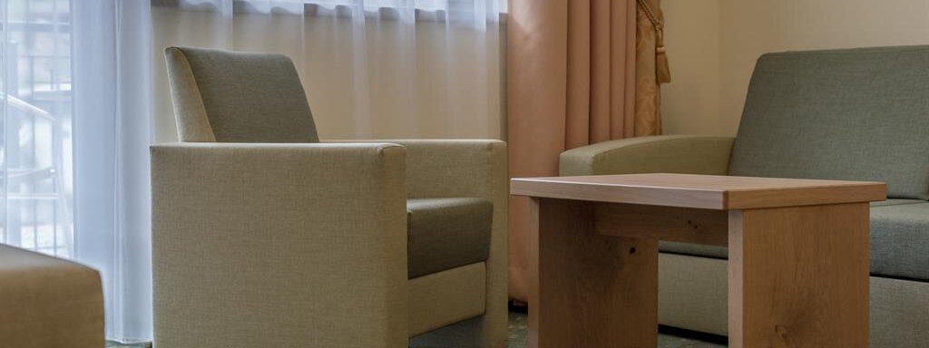 A cozy living space with a wooden coffee table and comfortable armchairs. Large windows let in plenty of daylight. - Residenz Allegra - Sölden