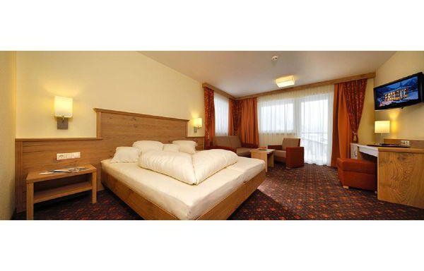 A cozy hotel room with a large bed, a table, and a seating area. There are windows with curtains and a television on the wall. - Residenz Allegra - Sölden