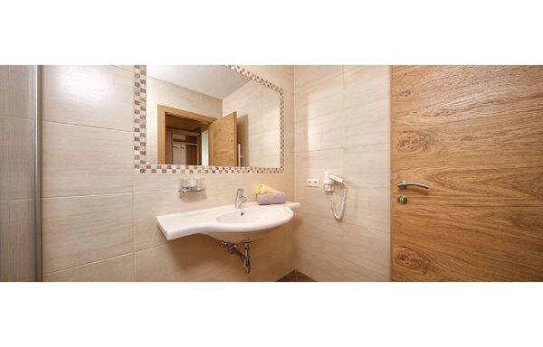 A modern bathroom with a sink and a large mirror. The walls are brightly tiled, and there is a wooden door in the background. - Residenz Allegra - Sölden
